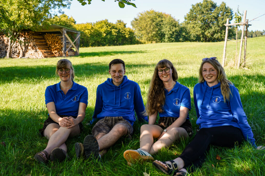 3 Frauen und ein Mann sitzen auf einer Wiese und tragen blaue Shirts und Hoodies.